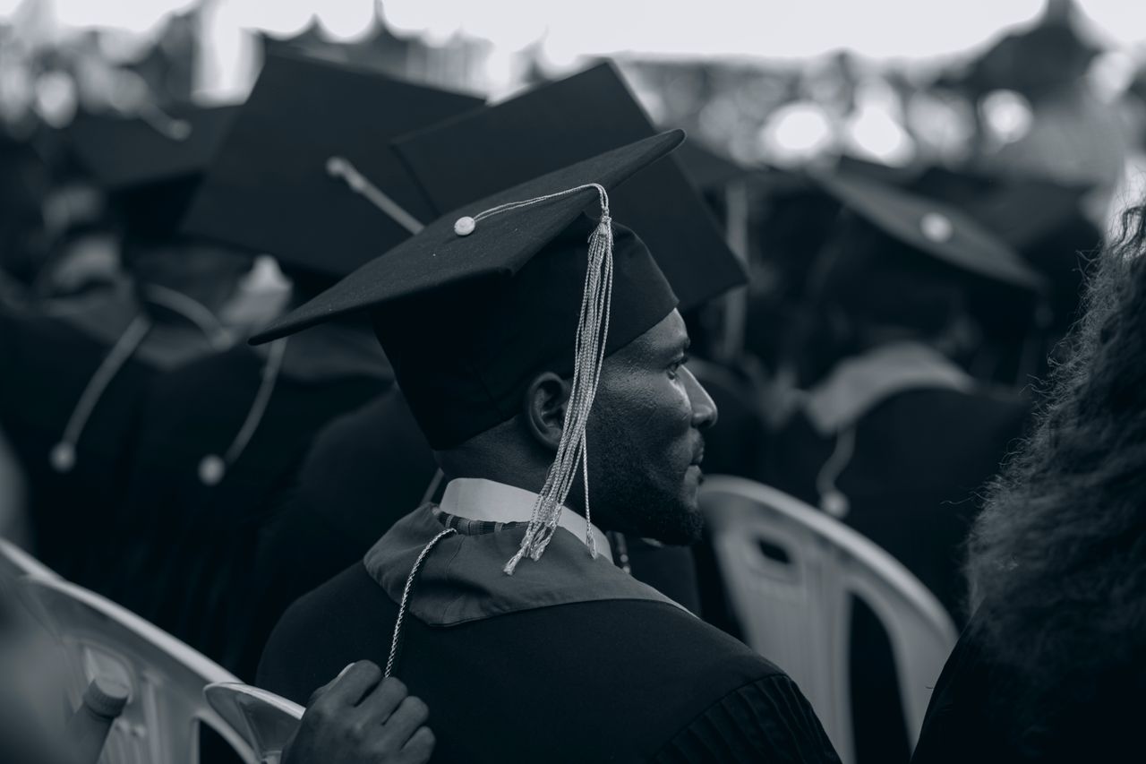 Black and white photo of graduates in caps and gowns at a ceremony.