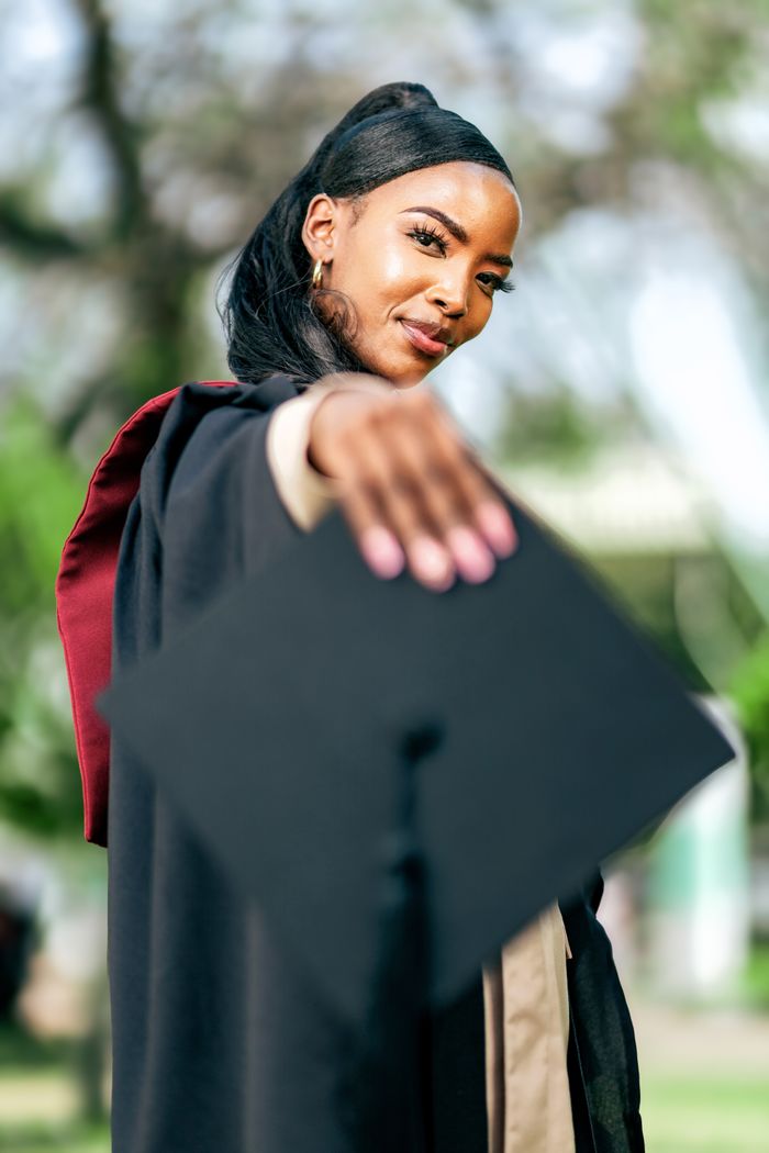 A proud graduate celebrating her achievement in an outdoor setting.