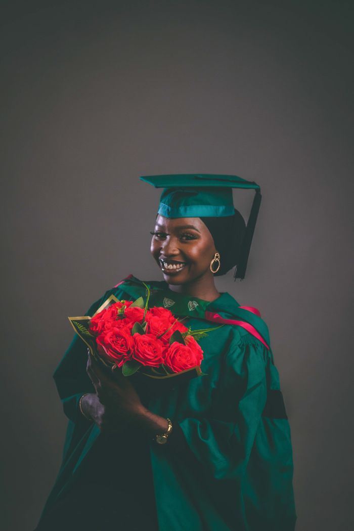 Smiling graduate with cap and gown holding bouquet of roses.