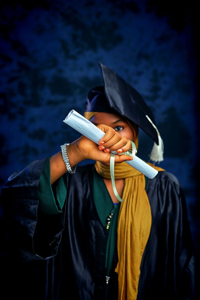 Young graduate holding diploma with pride in cap and gown.