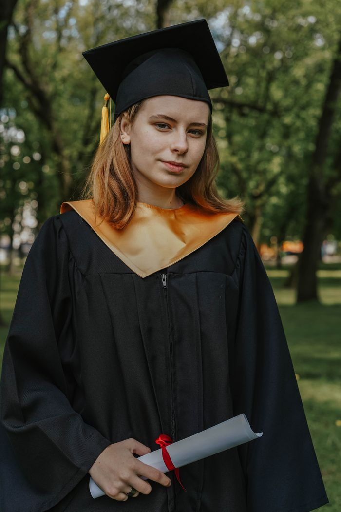 A young woman in a graduation cap and gown holding a diploma outdoors.